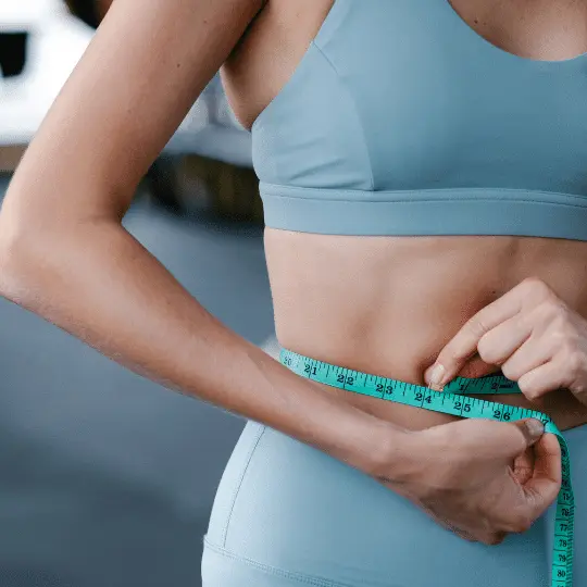 A fit woman measuring her waist with a measuring tape