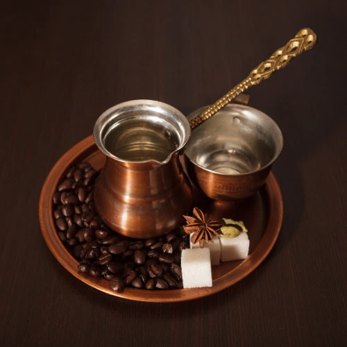 Copper coffee pot on a saucer with coffee beans and sugar cubes